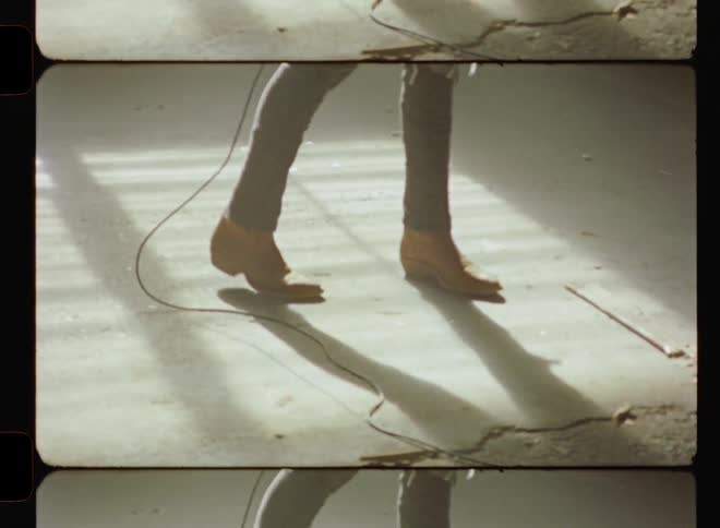 Person wearing cowboy boots walks on a floor dragging a cord