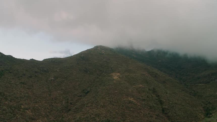 Rain clouds are drifting over a mountain peak in daylight