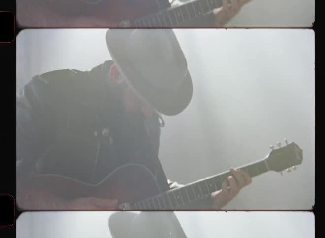 A man is playing a guitar inside an abandoned warehouse in daylight