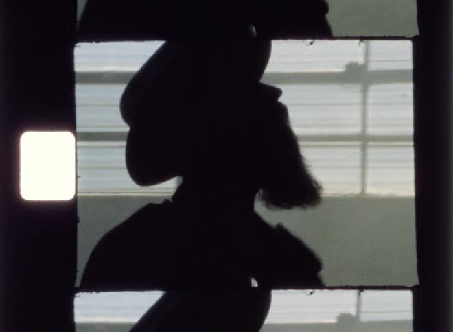 Man is walking and playing guitar next to a window inside building