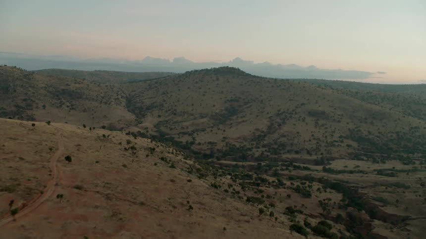 Trees and dirt cover a hilly landscape at sunset