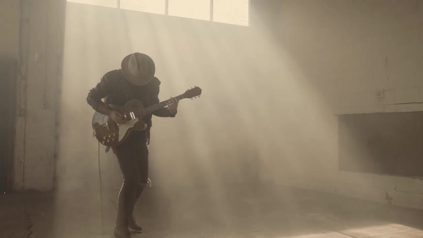 A man plays guitar in a dusty warehouse
