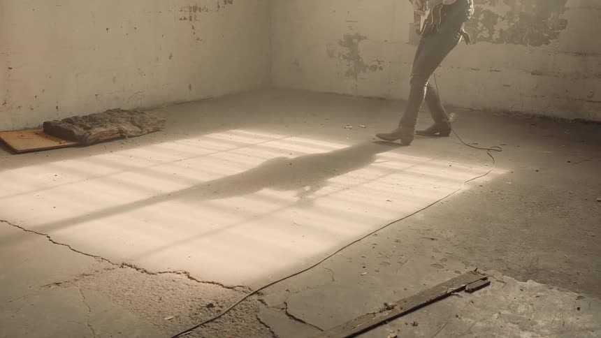 A man is playing a guitar inside an abandoned warehouse in daylight