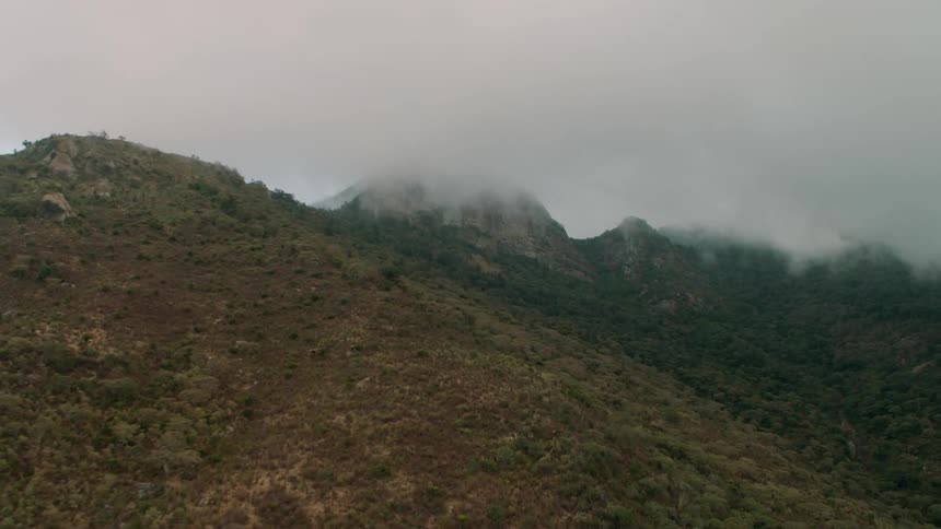 The clouds are touching the top of the green mountain