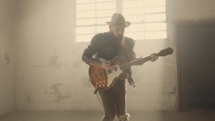 A man plays guitar as he jumps around in the warehouse