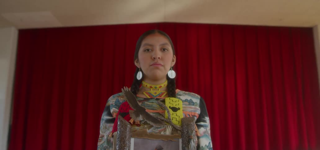 American indian woman standing in an auditorium holding a portrait and red curtains are closed behind her
