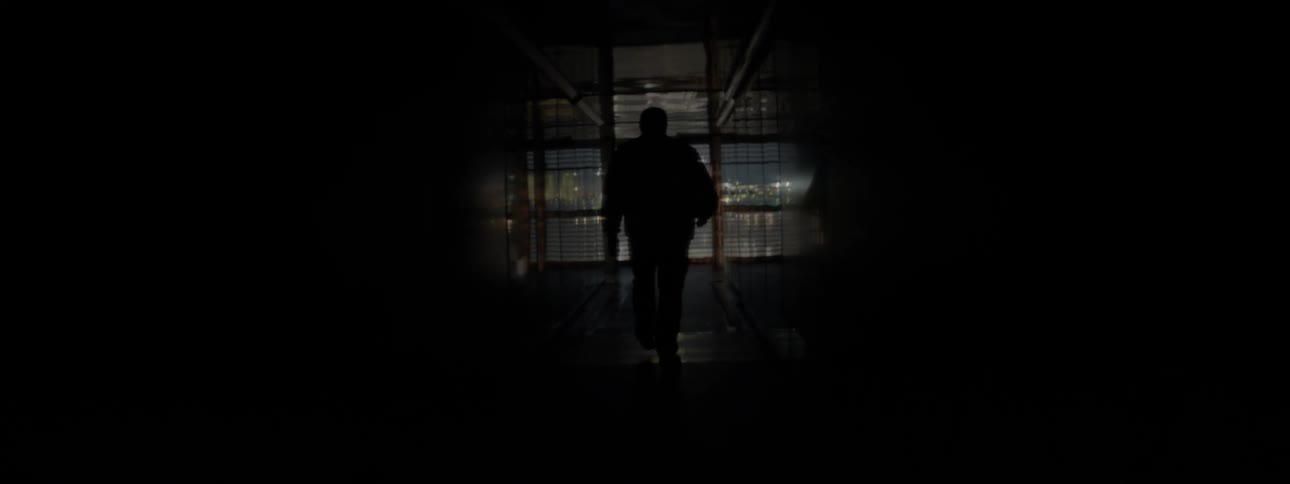 A man slowly walks down the very dark hall