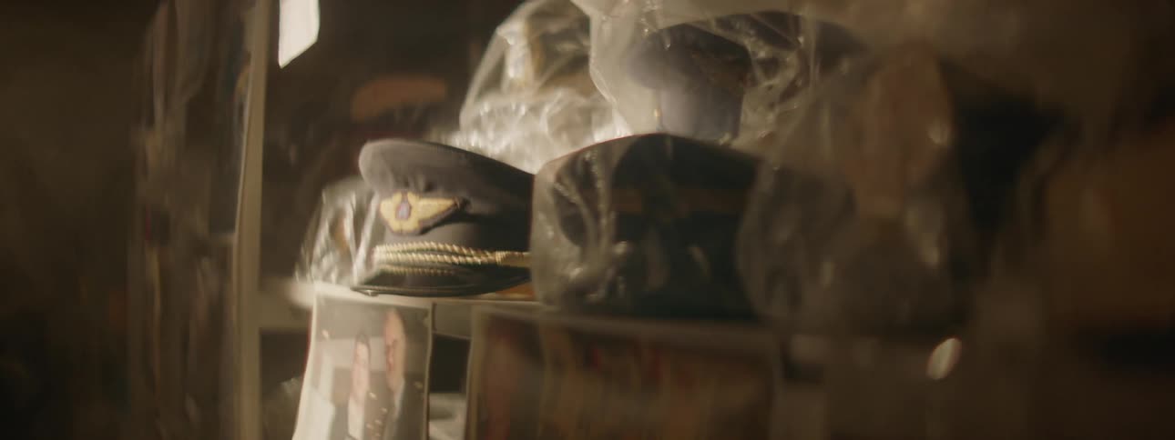 Military hats amongst other items in storage in a dimly lit area but some moving light shines across them
