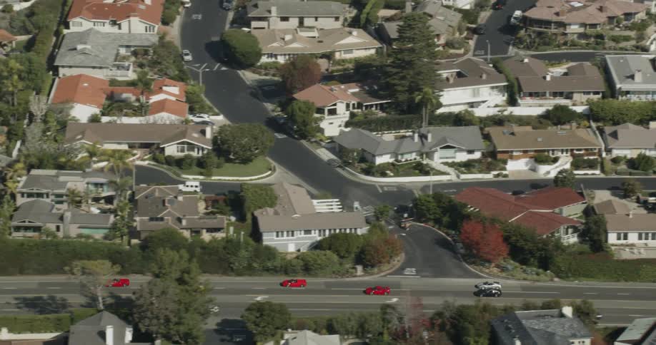 A group of luxury sports cars are driving on a road through a community in daylight