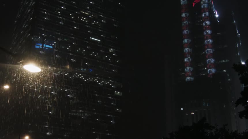 Rain is pouring down over a lamp post in a city at night