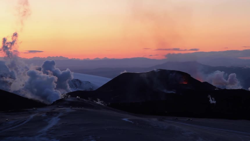 A helicopter flies over a volcano at sunset