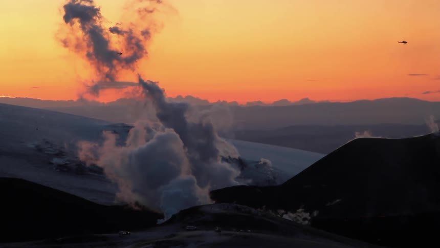Smoke is rising from the volcano as the helicopter flies past