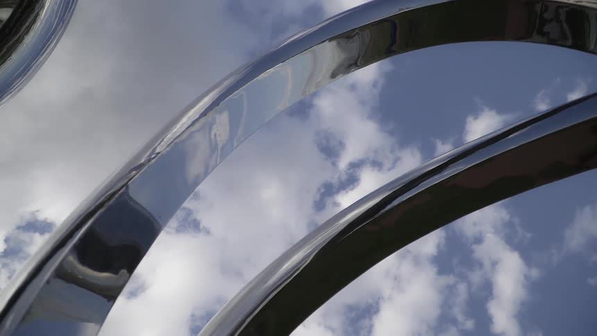 The sky and clouds are reflected in a metallic structure