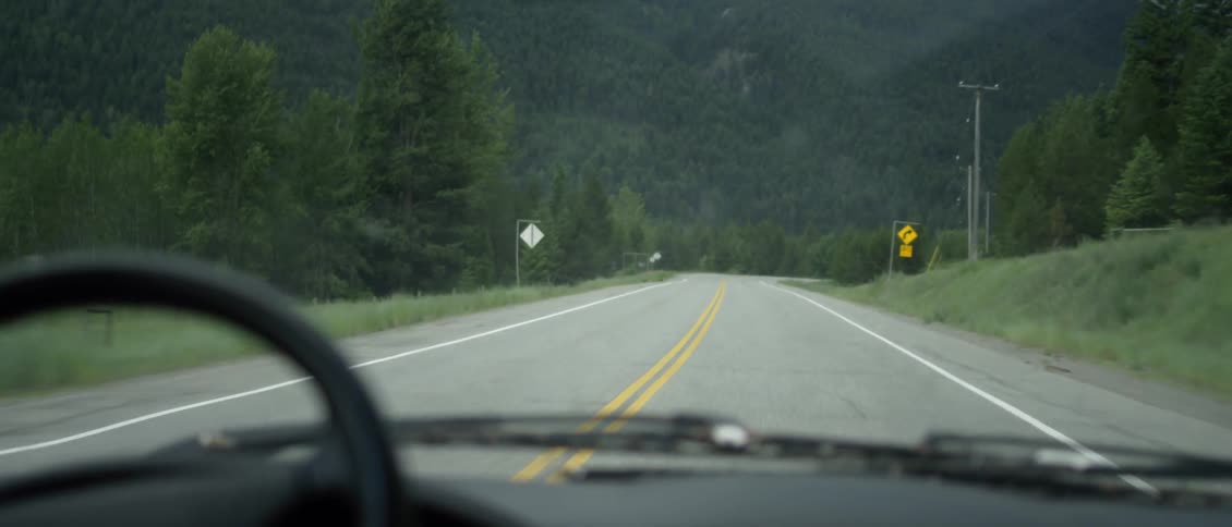 Person driving down a two-lane paved road as seen through the windshield