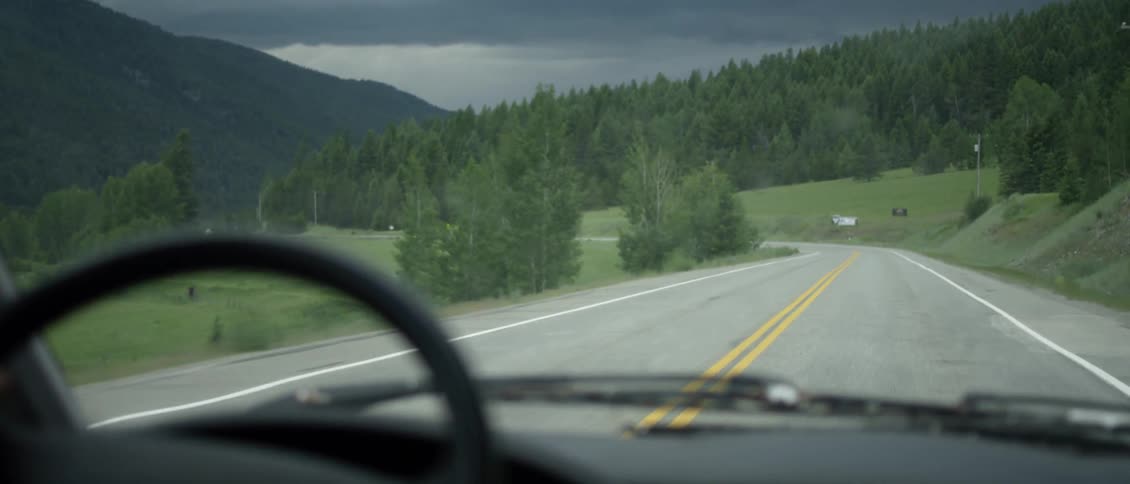 The car is driving towards the mountain on the road