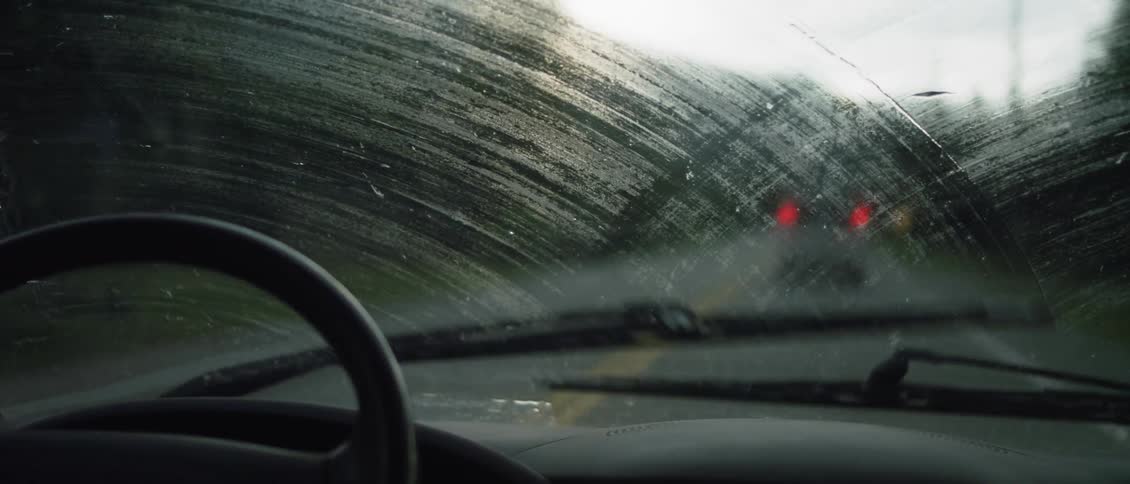 A vehicle is using its wipers as it is driven on a rural road in daylight