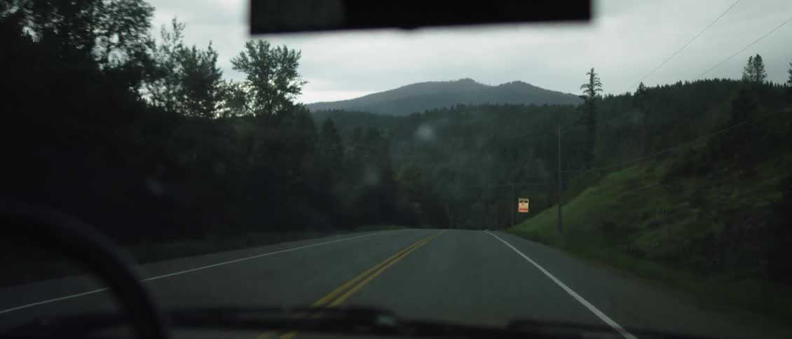 The car is traveling down the road on a cloudy day