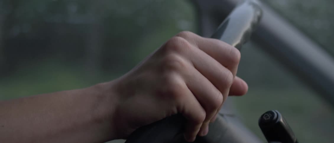 A man is gripping a steering wheel as he drives during the day