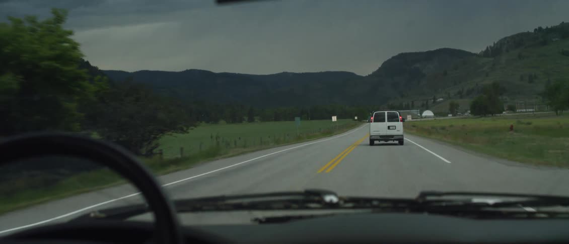 Car being driven as they follow a white van on a two-lane road on a cloudy day