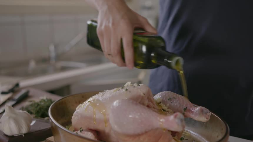 A person pours oil on a chicken in a pan