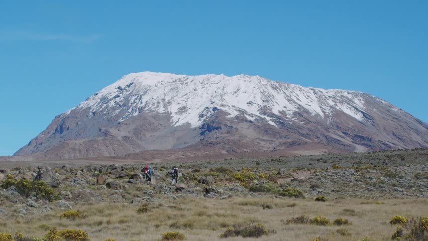 Two people hiking across a rocky area with mountains in the background on a clear day