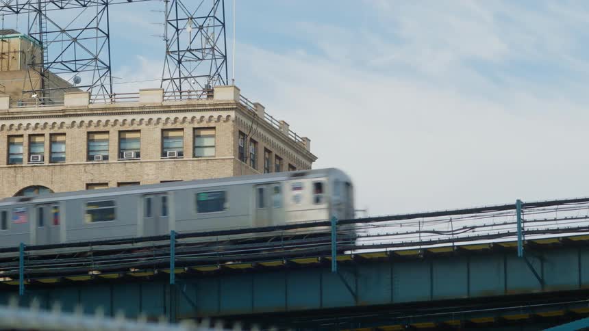 A train travels down a bridge in front of a large building