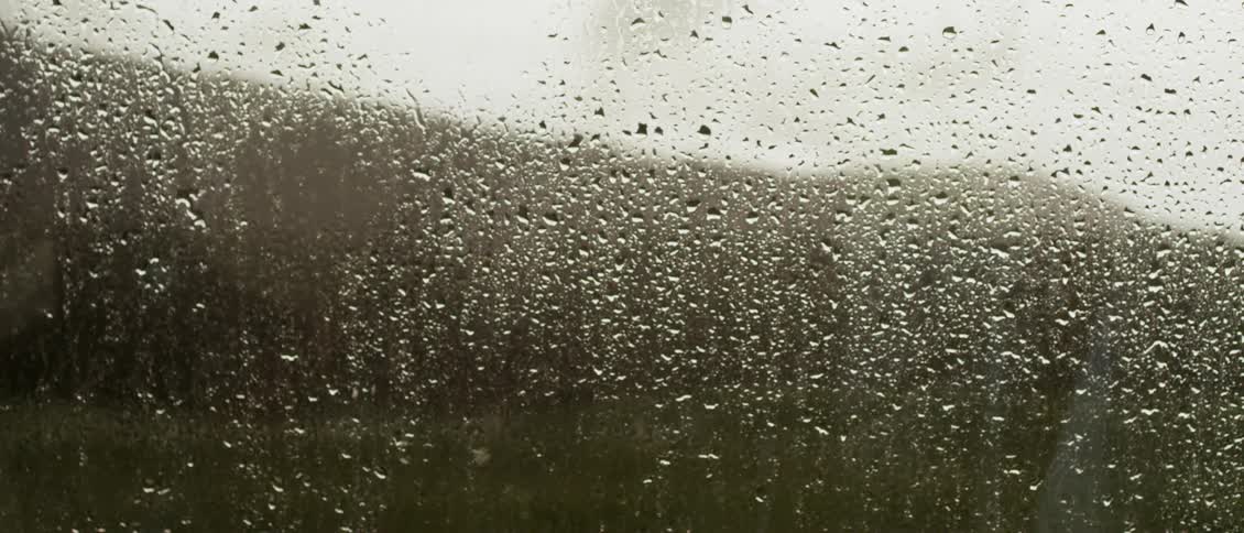 Raindrops are sliding down a vehicle windows as a truck rolls by on the road outside