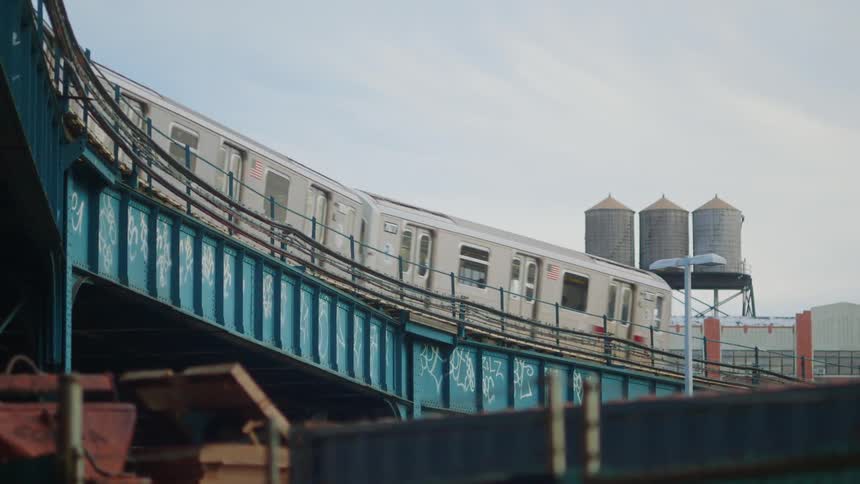 A commuter train is traveling on an elevated track in a city in daylight