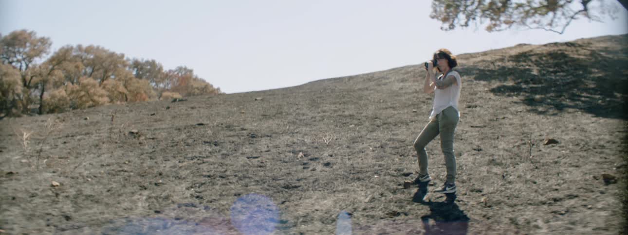 A woman is standing on a hill taking photographs