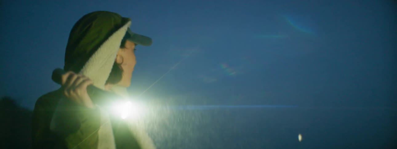 A woman uses a flashlight on the beach at night