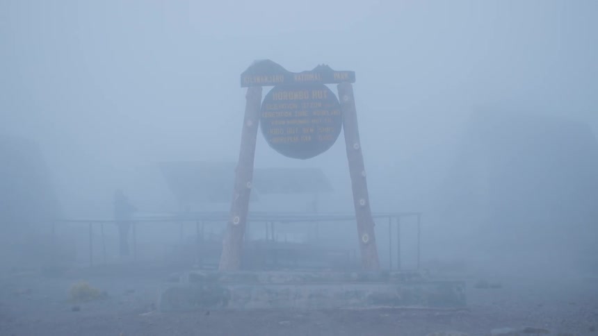 A sign and fence are barely seen through thick fog