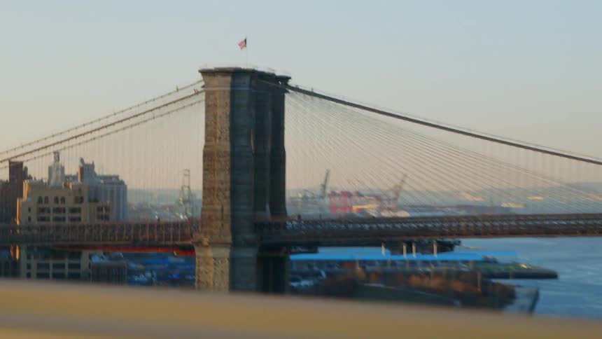 An american flag is flapping in the breeze atop a bridge outside a city on a sunny day