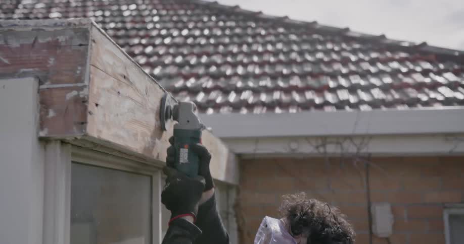 A man sands a wood facade on a house