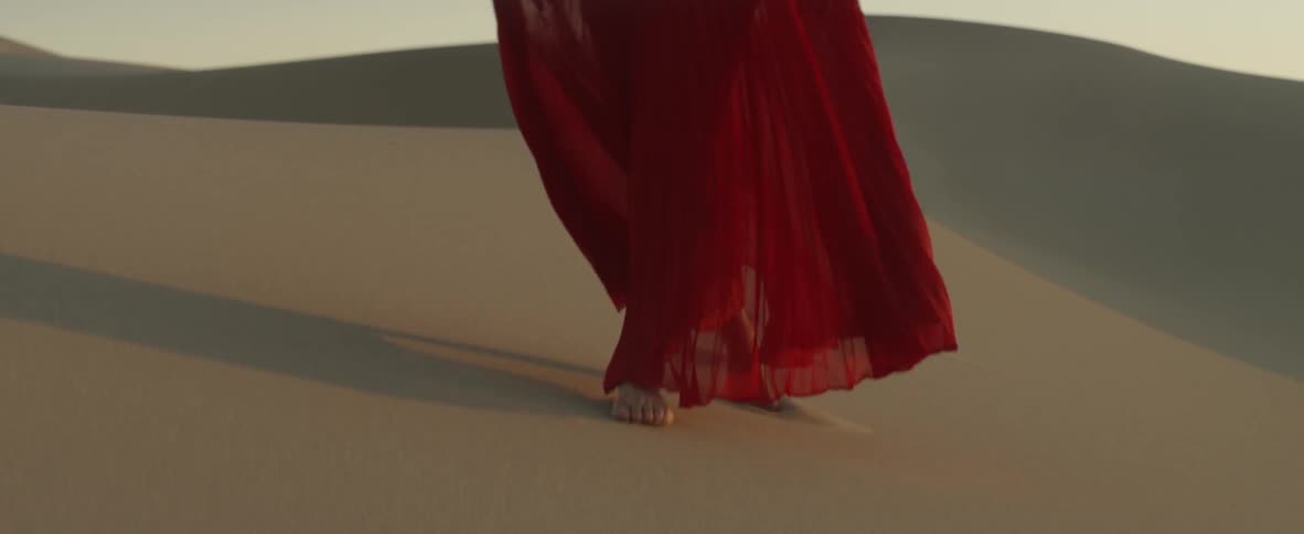 A woman in a red dress walks on the sand