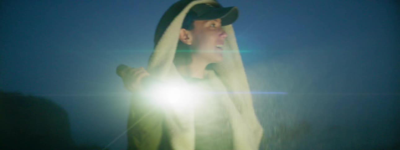 A woman shines a flashlight on the beach at night