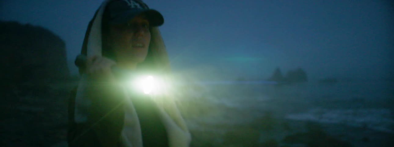 A woman with a flashlight is walking next to the ocean