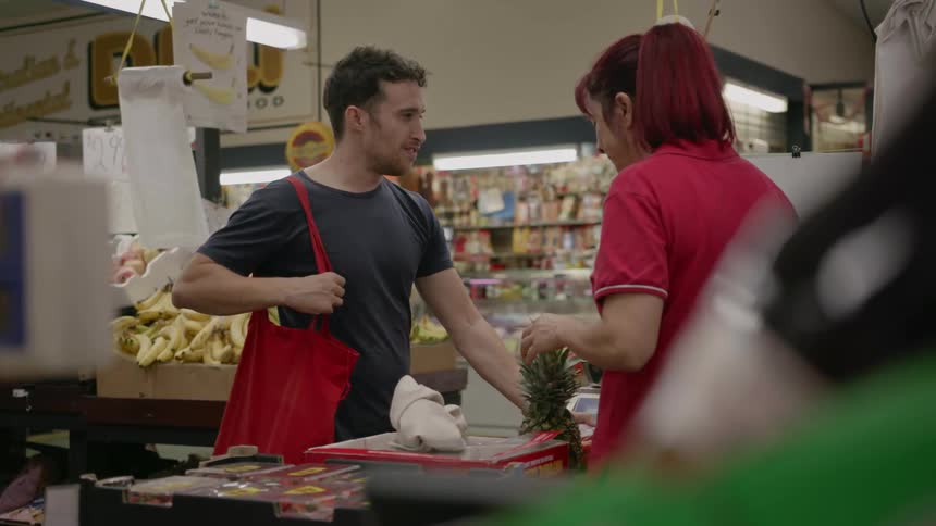 A man is talking to a cashier as he purchases groceries