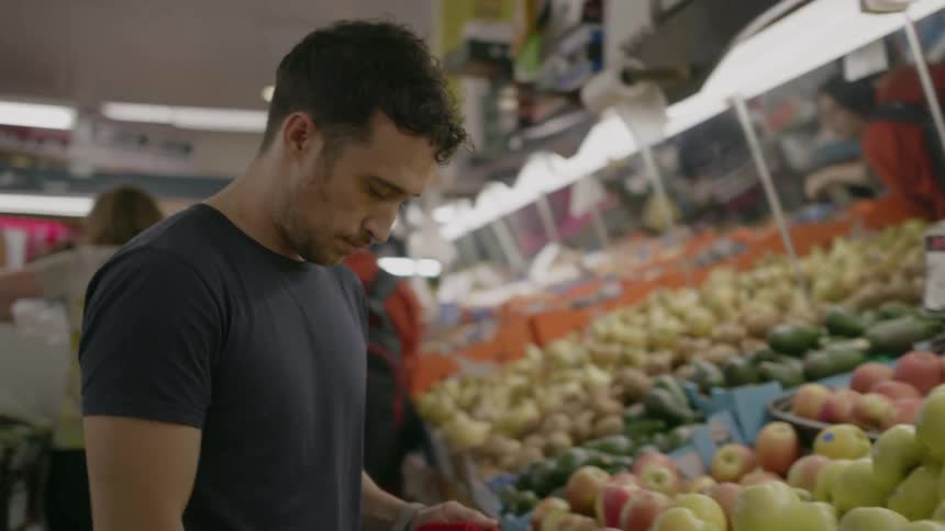 Man shopping at a grocery store puts apples in a red backpack