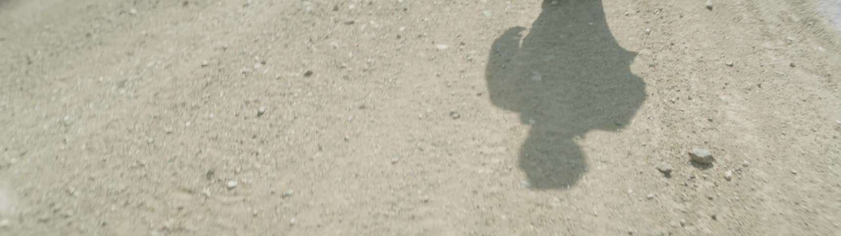 The shadow of a man walking a dirt road on a sunny day