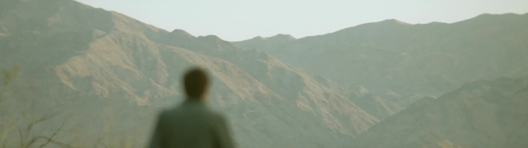 A man walks outside under the sun near tall mountains