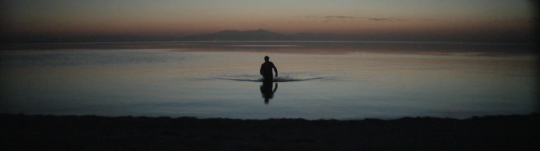 Man wearing clothes wading towards the shore from the sea around sunset
