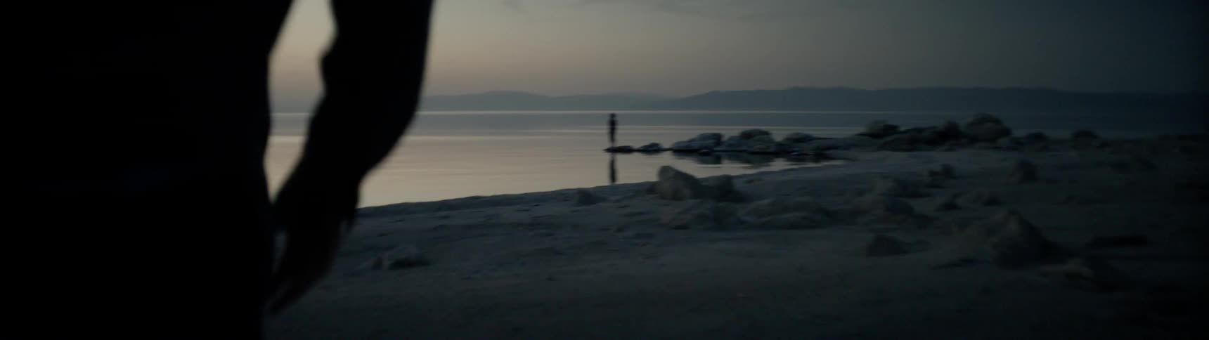 A man walks on a lakeshore at sunrise
