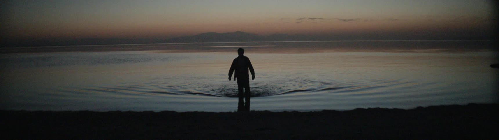 A man wades in the water at dusk