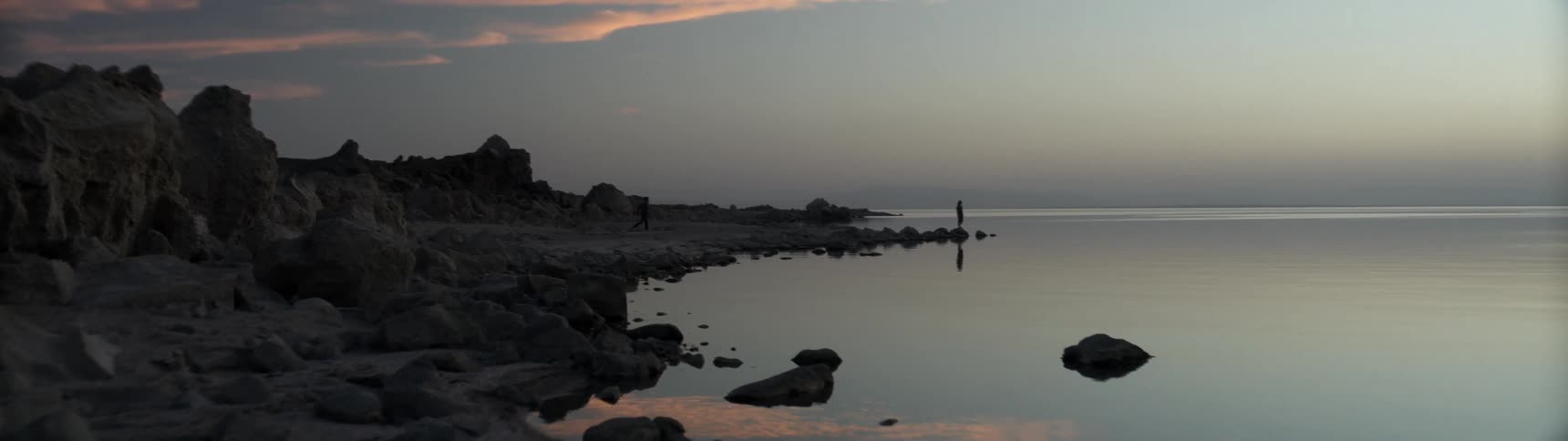 Person standing on the edge of a row of rocks looking out to the sea on a cloudy day