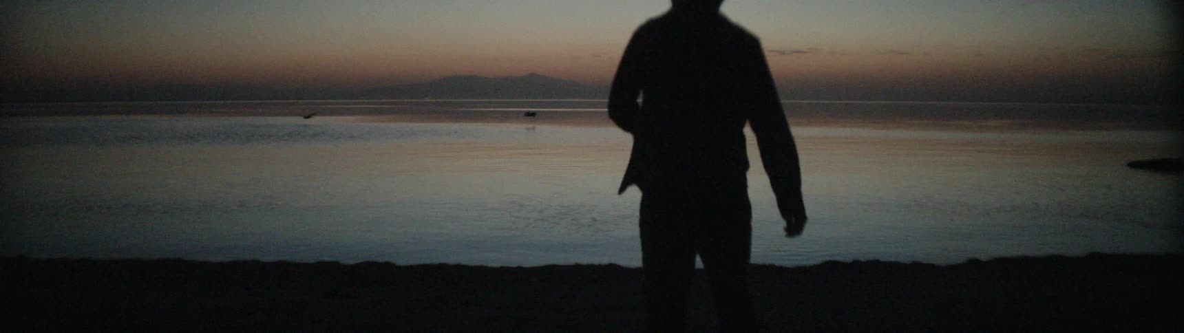 A woman walks on the rocky shore