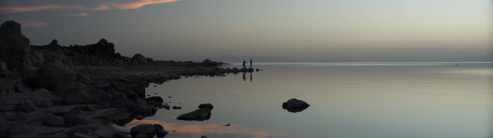 Two people stand on a lakeshore at sunrise