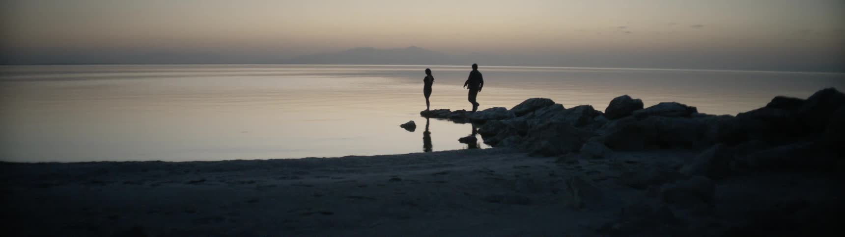 Two people walk on the rocks near the beach