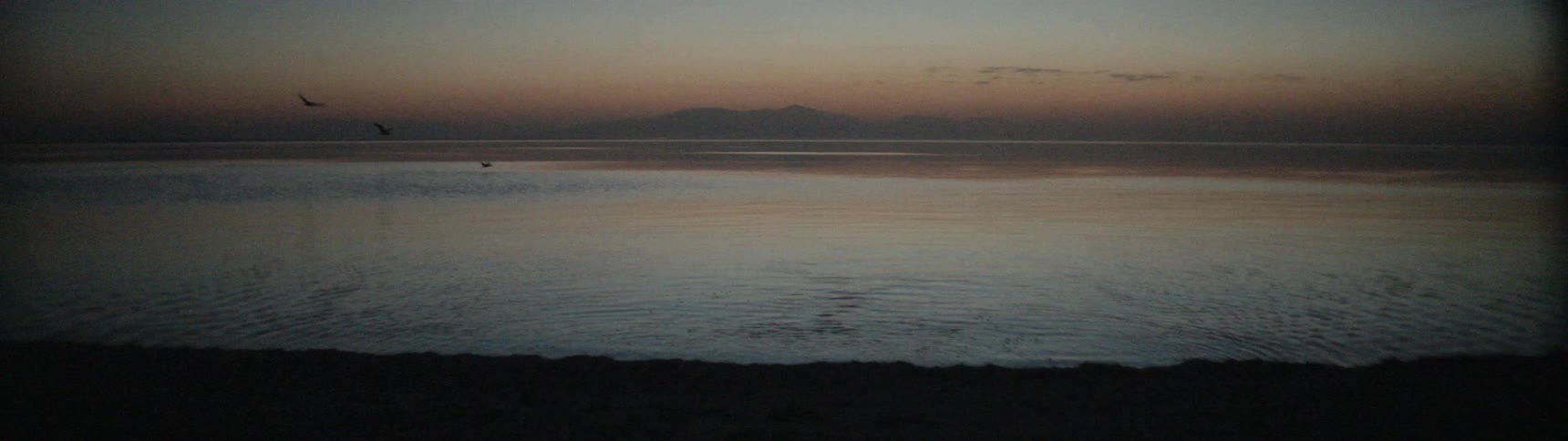 A person walks from the shore at sunset