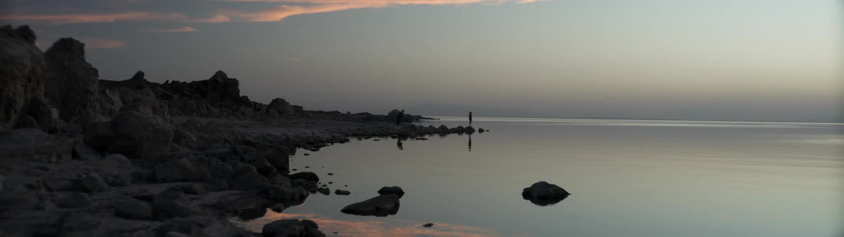 Two people walk on the rocky beach shore
