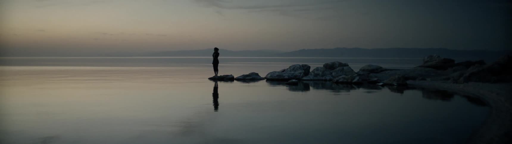 A woman stands on a lakeshore at sunrise